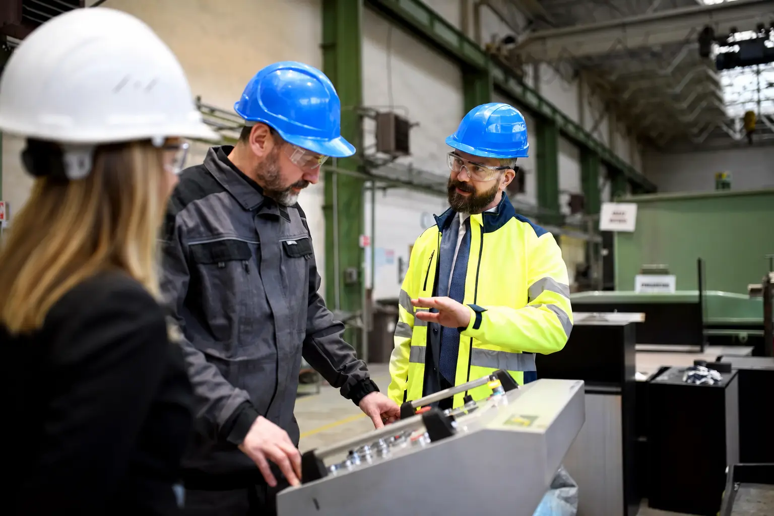 Three workers talking over machine